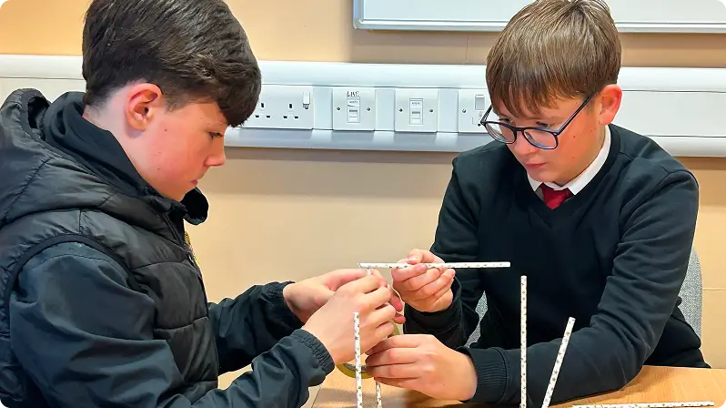 Two young boys building a structure out of straws.